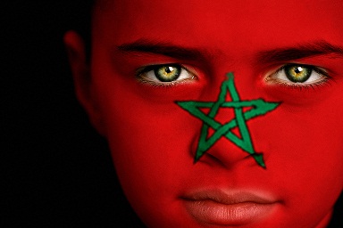 Portrait of a boy with the flag of Morocco painted on his face.